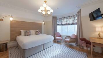 A hotel room with a large bed, a desk, a chair, a television, and a chandelier.