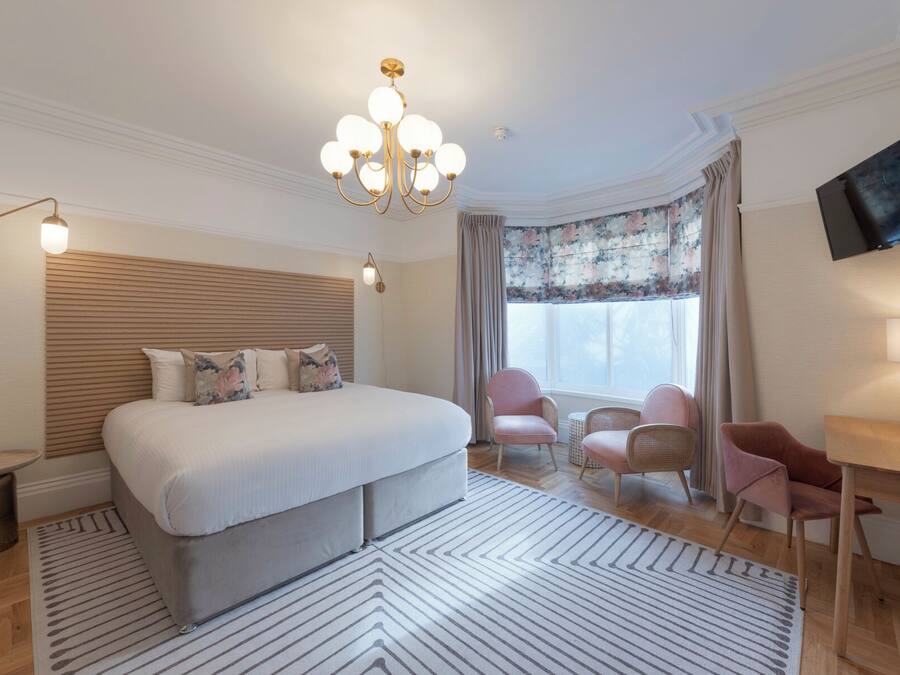 A hotel room with a large bed, a desk, a chair, a television, and a chandelier.