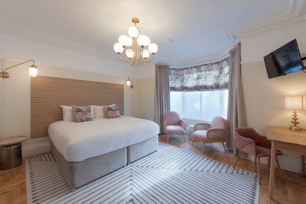 Una habitación de hotel con una cama grande, un escritorio, una silla, un televisor y una araña.