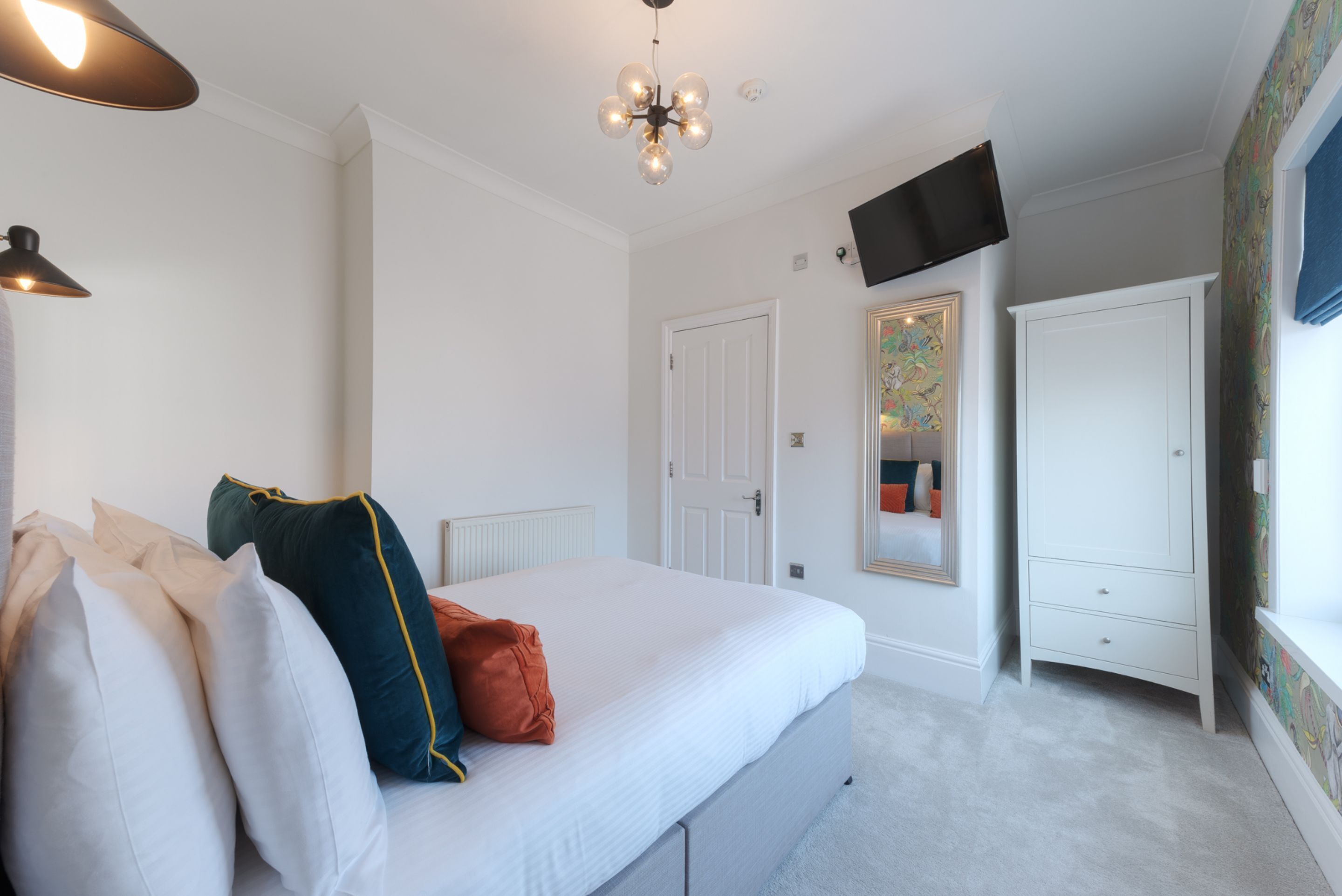 A bedroom with a bed, a wardrobe, a television on the wall, and a window with curtains.