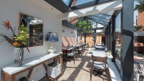 A sunlit room with a large skylight, a mirror, a vase with flowers, and a table with chairs.
