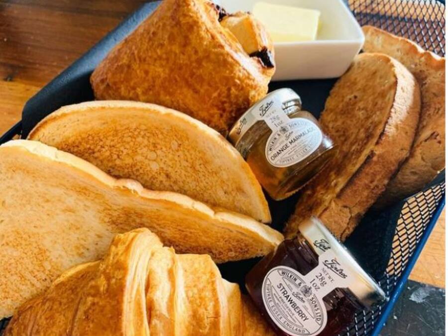 A tray with various types of bread and two bottles of jam.