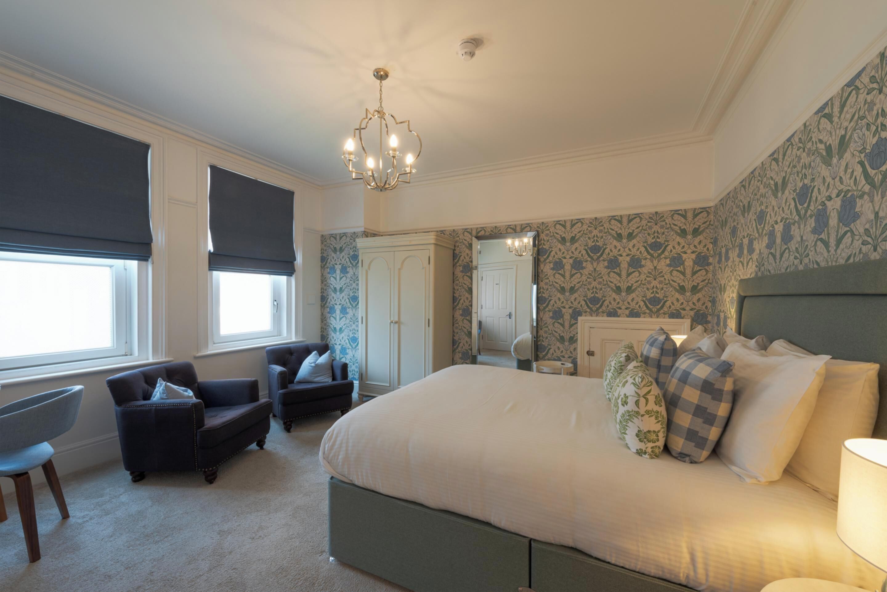 A bedroom with a large bed, a chair, a desk, and a wardrobe.
