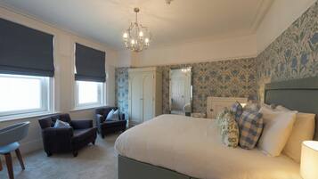 A bedroom with a large bed, a chair, a desk, and a wardrobe.