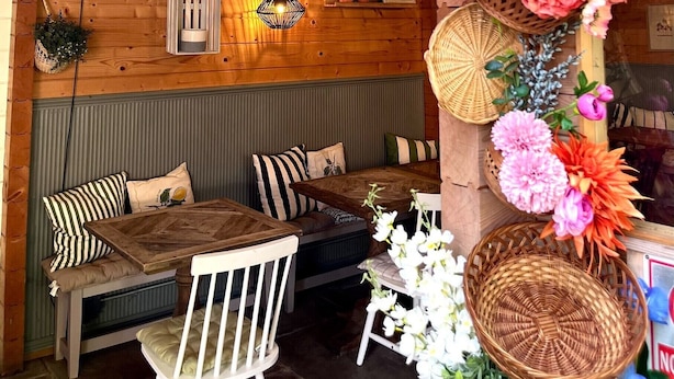 A cozy wooden interior with a seating area, wicker baskets, and various flowers.