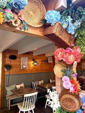 Un interior de madera acogedor con una zona de estar, cestas de mimbre y diversas flores.