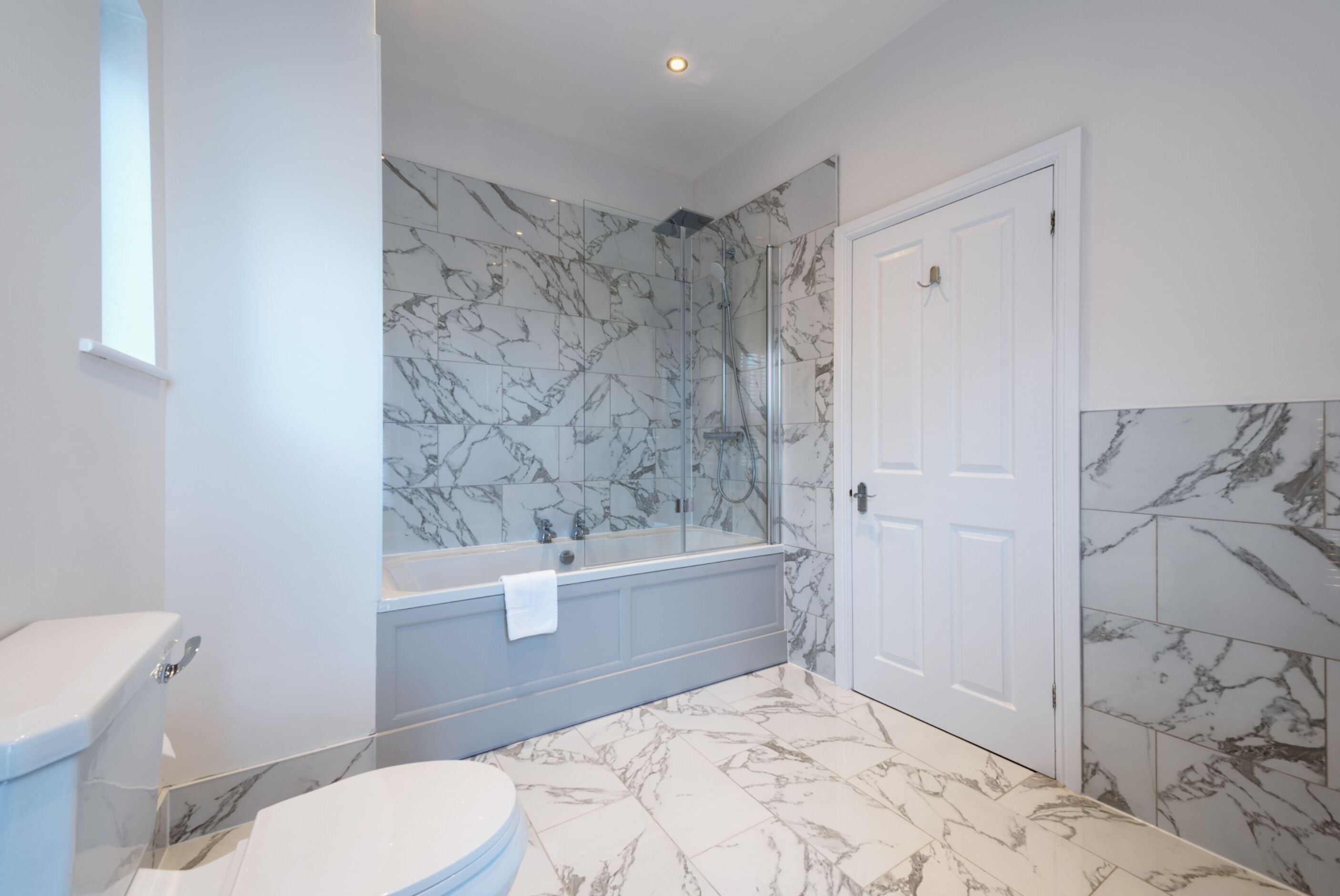 A bathroom with a toilet, a bathtub with a glass enclosure, and a shower area.