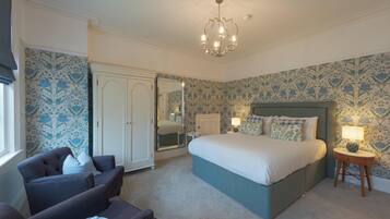 A bedroom with a large bed, a chair, a wardrobe, and a chandelier.