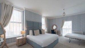 A bedroom with a large bed, bedside tables, a mirror, and a chair.