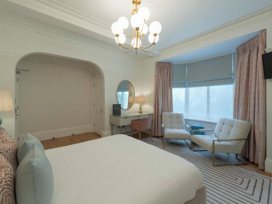 Ein Hotelzimmer mit einem großen Bett, einem Schreibtisch mit Stuhl, einem Fernseher und einem Fenster mit Vorhängen.