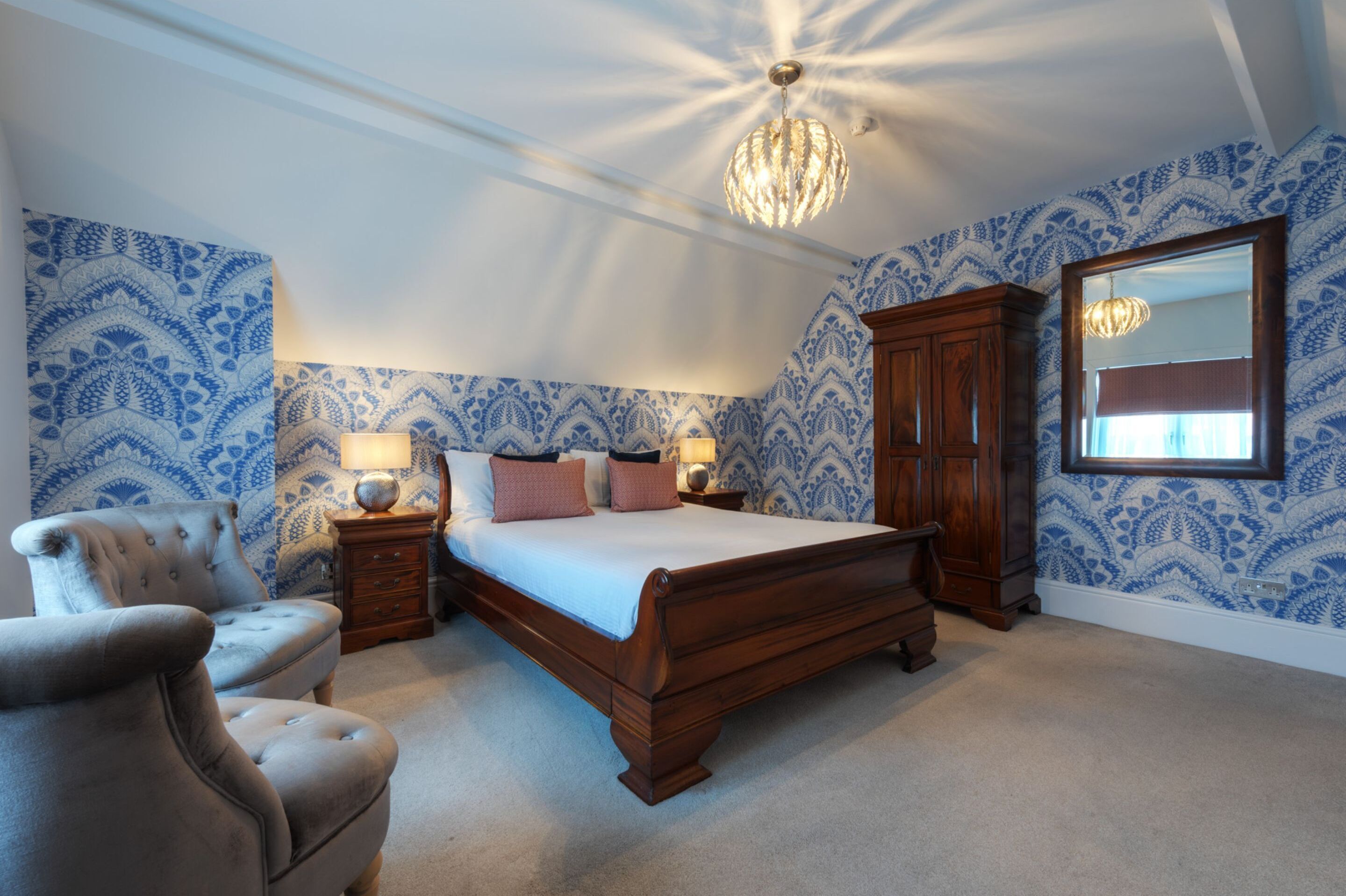 A bedroom with a large bed, two bedside tables, a nightstand, a wooden wardrobe, and a mirror on the wall.