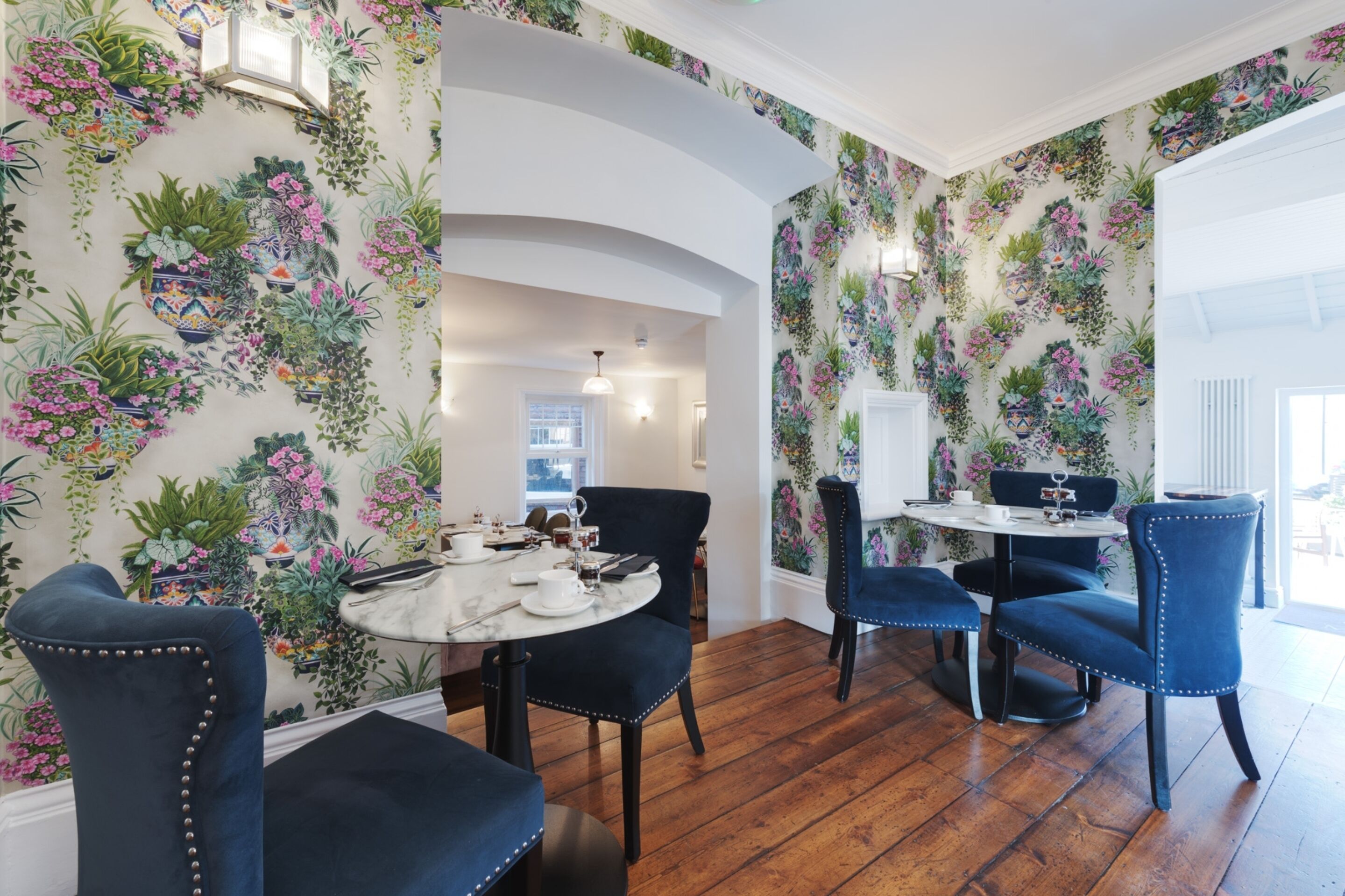 A dining area with a round table, blue upholstered chairs, and a floral wallpaper design.