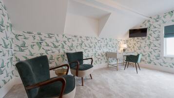 Una habitación con techo inclinado, dos sillones tapizados en verde, un escritorio pequeño y un televisor montado en la pared.
