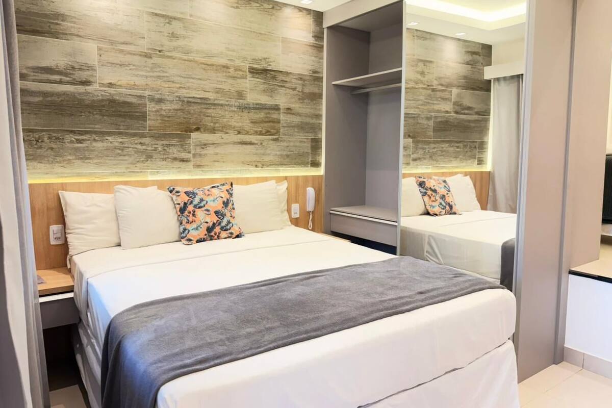 A modern hotel room with a large bed, a bedside table, a mirror, and a wardrobe.