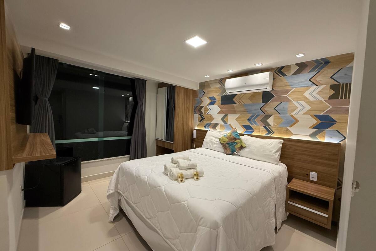 A modern hotel room with a large bed, a bedside table, a mirror, and a geometric-patterned wall.