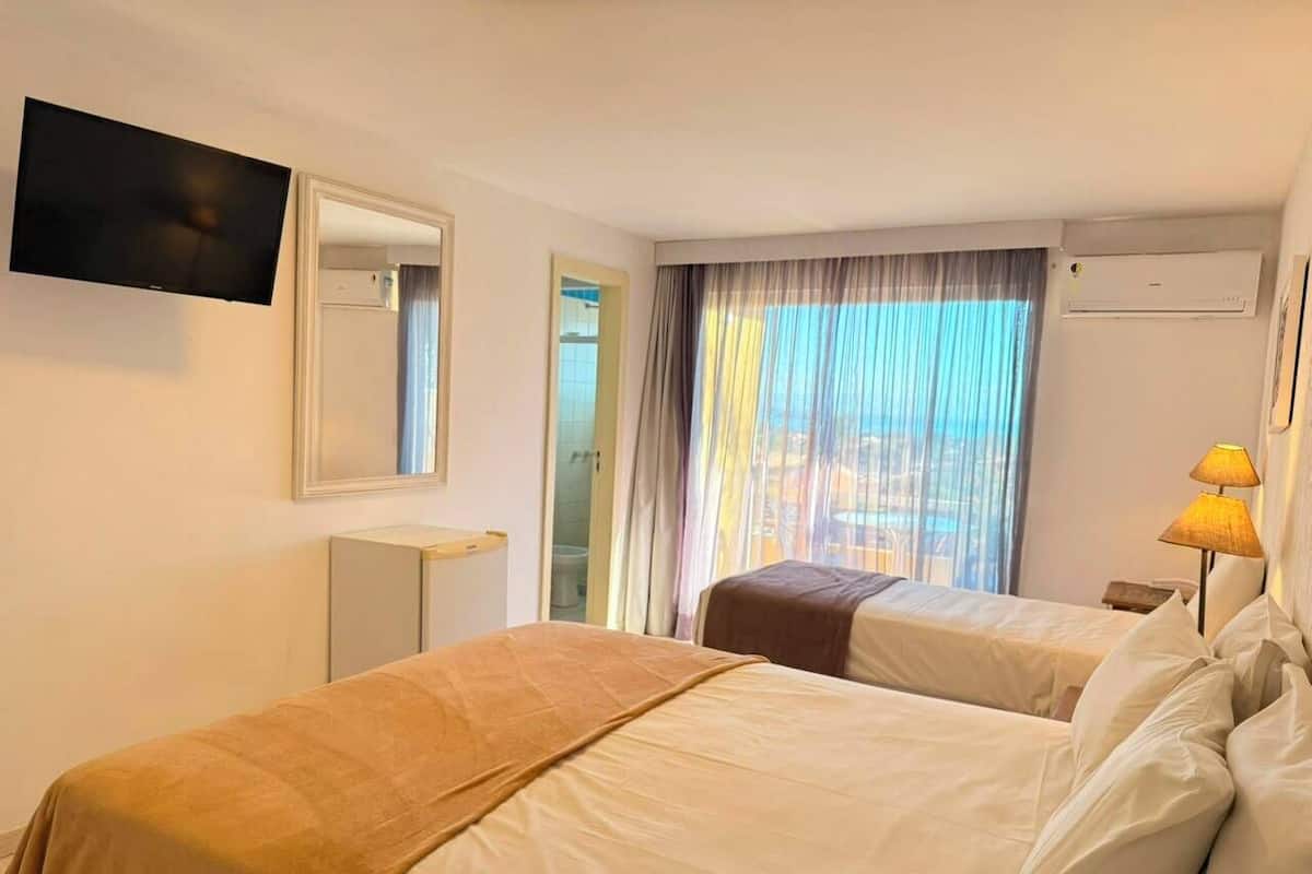 A hotel room with two beds, a TV, a window with curtains, and a lamp.