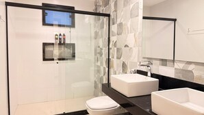 Un baño moderno con ducha acristalada, dos lavamanos y un inodoro.