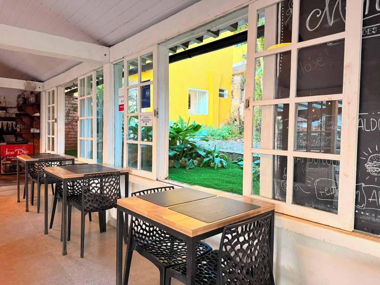 Un café con mesas al aire libre, pared amarilla y menús en pizarra.
