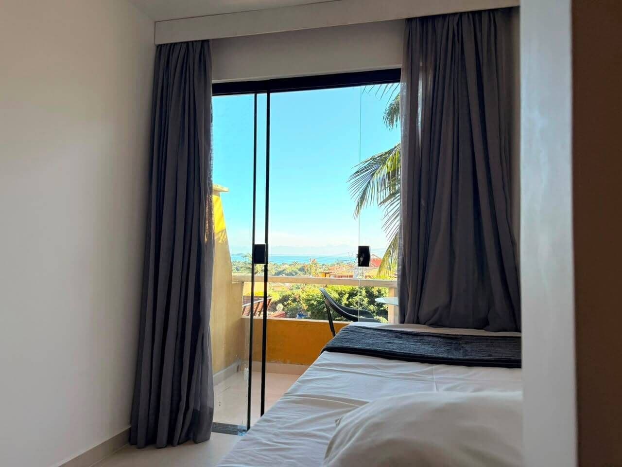 Une chambre dotée d’un lit, d’une porte-fenêtre coulissante donnant sur un balcon avec vue sur la verdure et un paysage lointain.