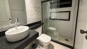 Un baño moderno con un espejo grande, un lavabo blanco, un inodoro y una zona de ducha con paredes de cristal.