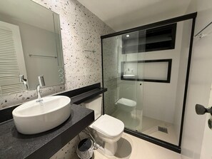 A modern bathroom with a large mirror, a white sink, a toilet, and a glass-enclosed shower area. - Pousada Casacolina (Búzios)