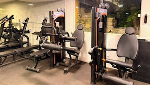 A gym with various exercise machines, a stone wall, and a large window. - Pousada Casacolina (Búzios)