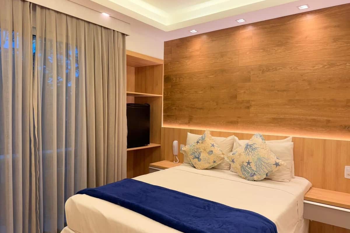 A hotel room with a bed, a television, a wooden headboard, and a curtain.
