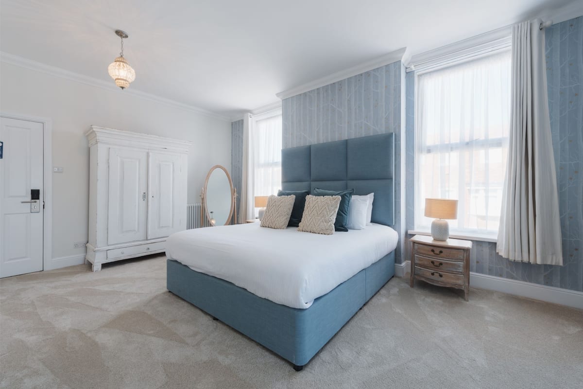 A bedroom with a large bed, a wardrobe, a nightstand, and a chandelier.