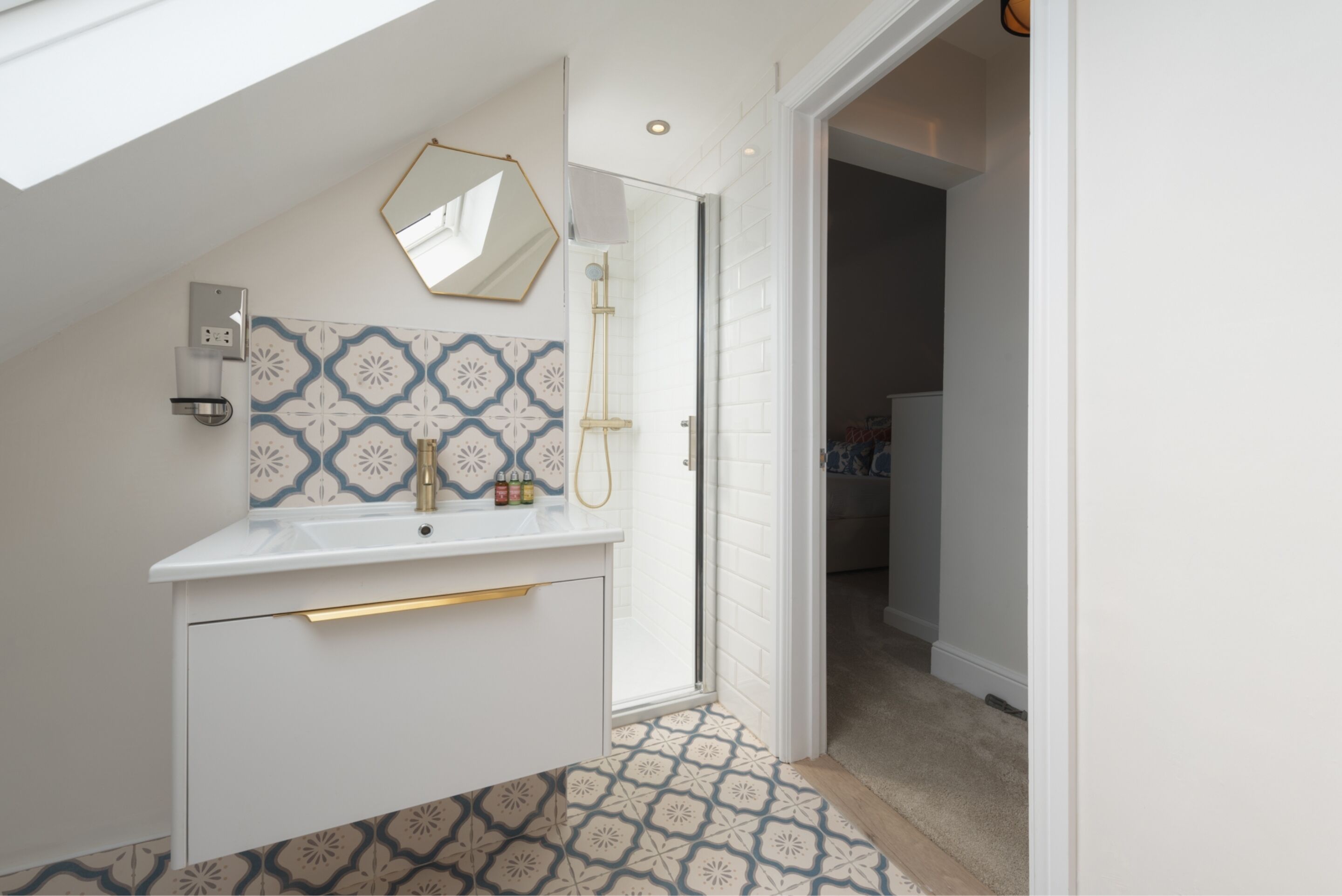 A modern bathroom with a white vanity, patterned tiles, a shower, and a skylight.