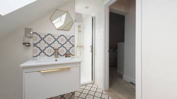 A modern bathroom with a white vanity, patterned tiles, a shower, and a skylight.