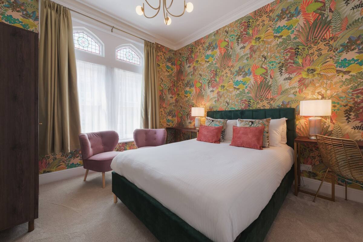 A bedroom with a large bed, two bedside lamps, a chair, and a wardrobe.