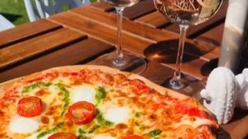 A pizza on a wooden table with two glasses of white wine.