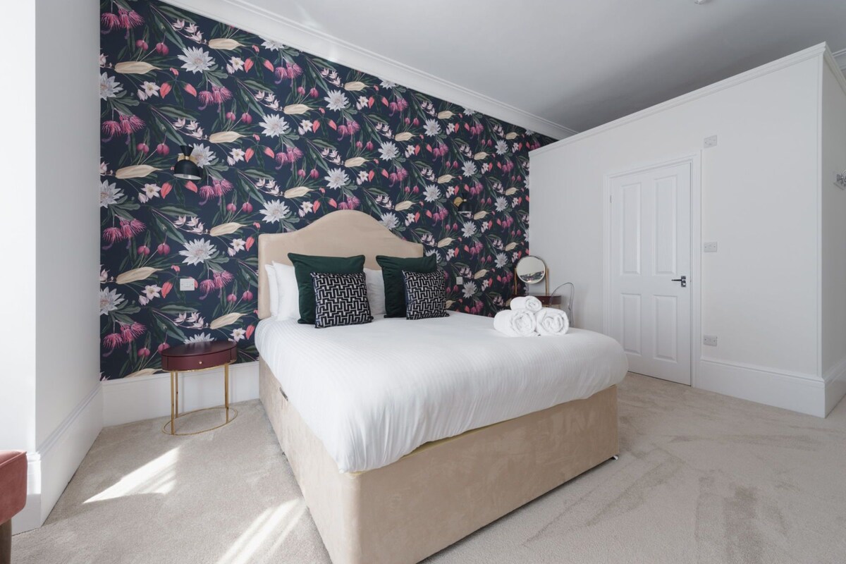 A bedroom with a bed, a bedside table, a mirror, and a door.