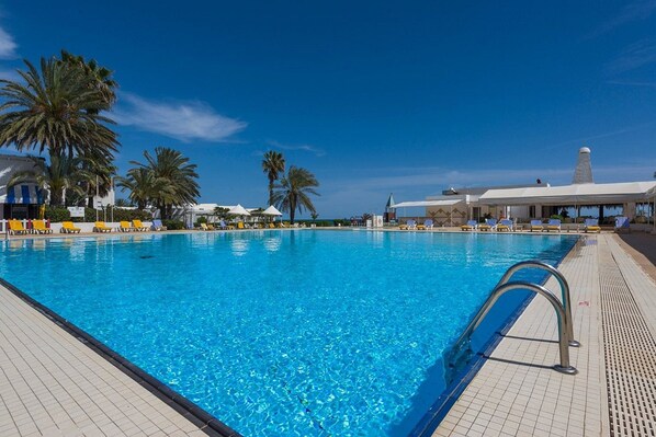 A clear blue pool with lounge chairs and palm trees.