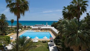 Um resort com piscina, palmeiras e vista para o oceano.