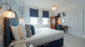 A bedroom with a bed, bedside lamp, dresser, desk, chair, and a TV. - Florence Gardens Hotel & Restaurant (Portsmouth)