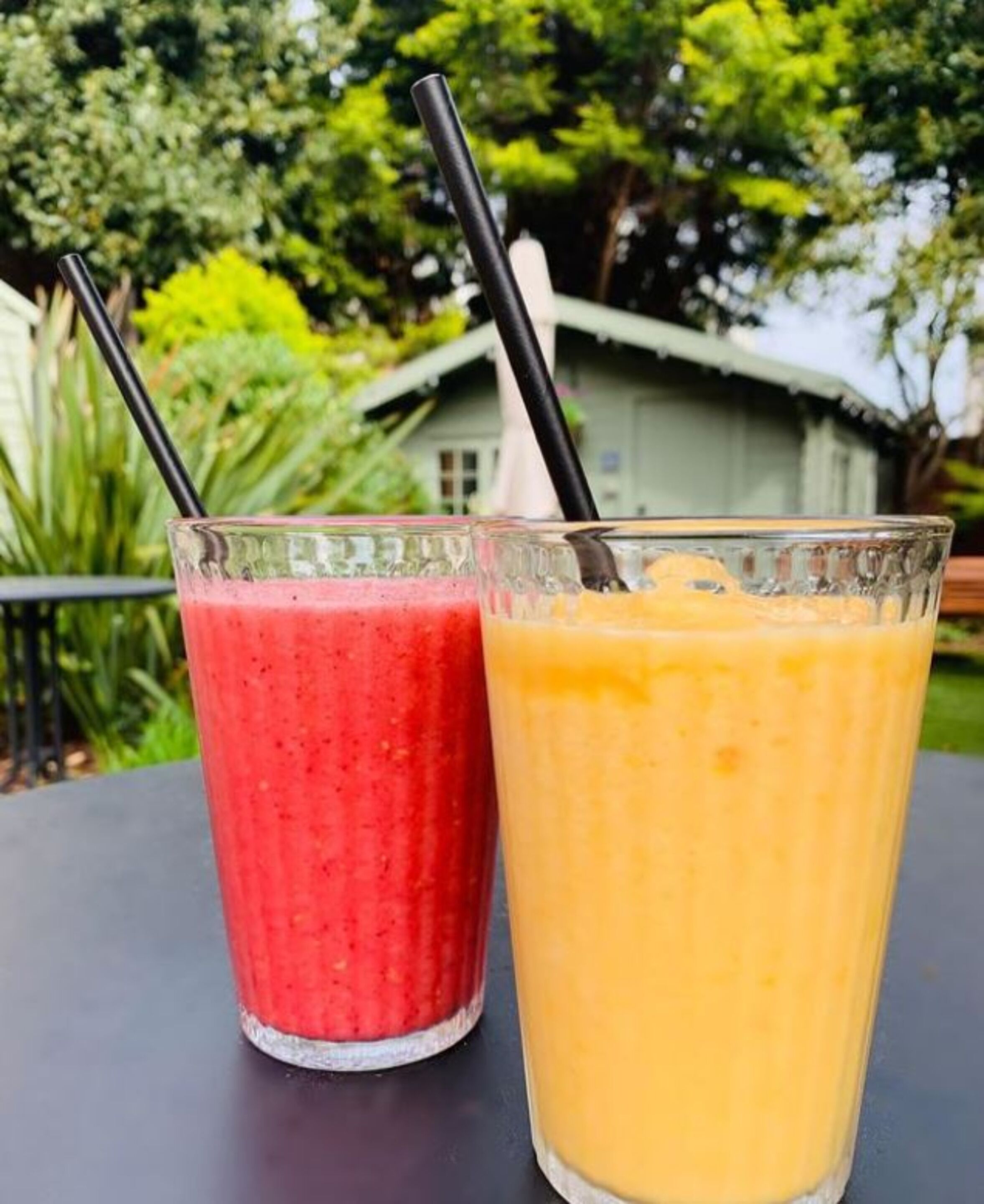 Two glasses of smoothies on a table with a black straw in each.