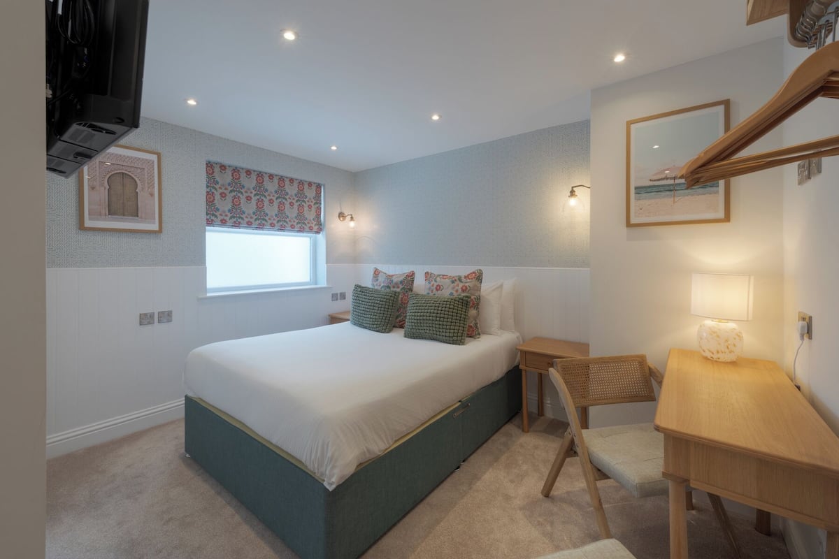 A bedroom with a bed, bedside table, lamp, and a window with a floral curtain.