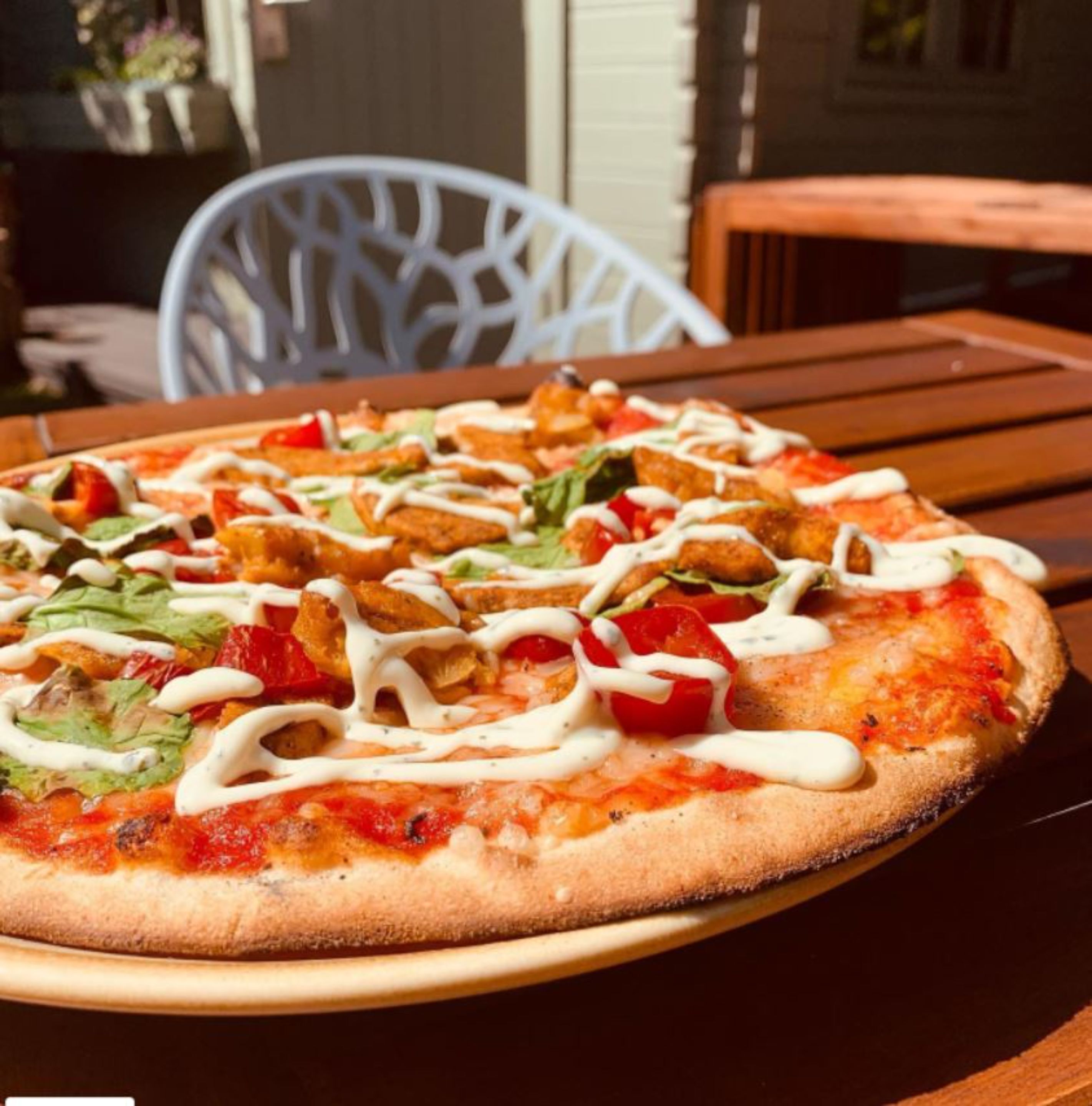 A pizza with various toppings and a white sauce, served on a wooden table.