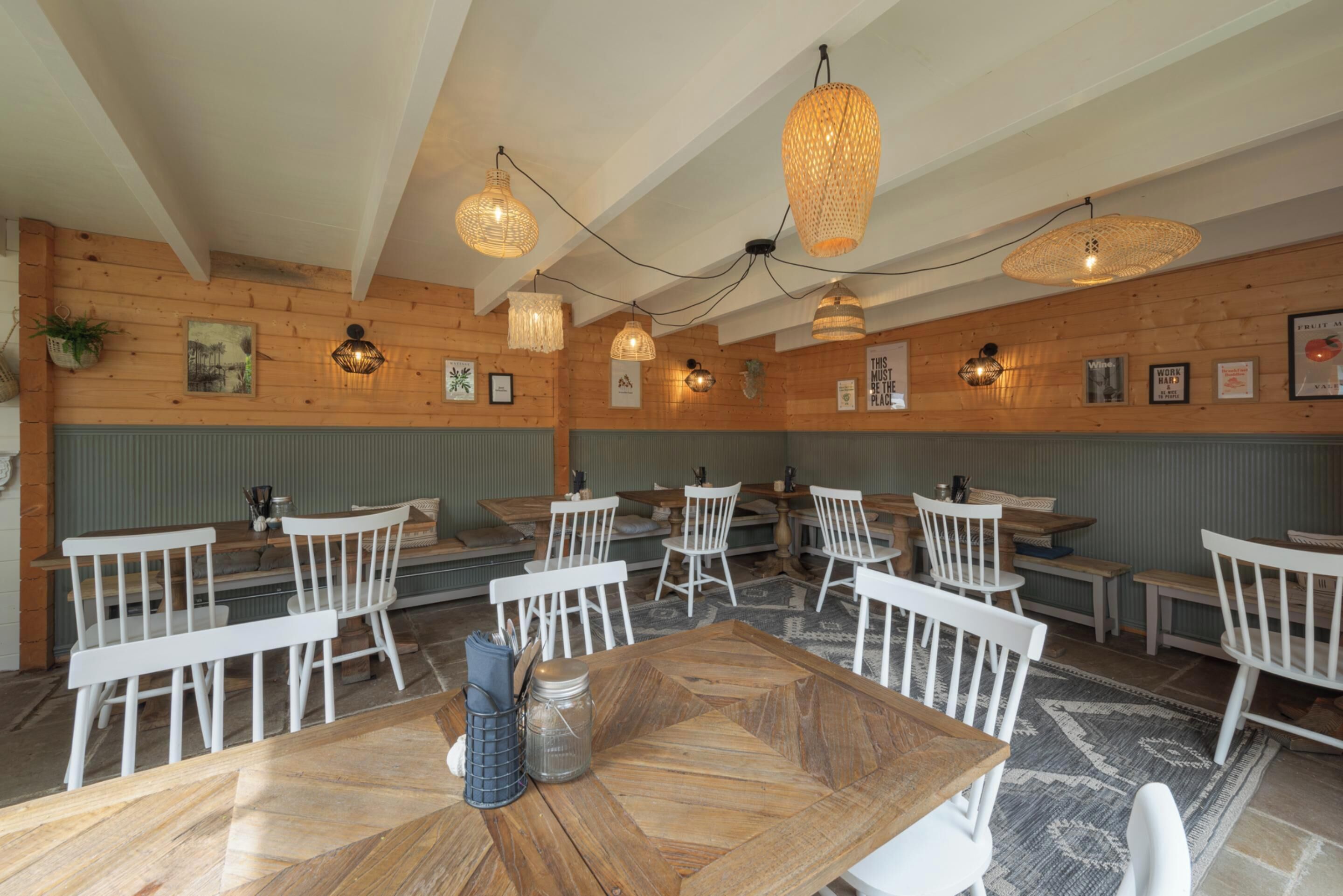 A restaurant with wooden walls, white chairs, and tables. There are string lights hanging from the ceiling.