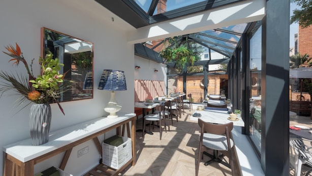 A sunlit room with a large skylight, a mirror, a vase with flowers, and a table with chairs. - Florence Gardens Hotel & Restaurant (Portsmouth)