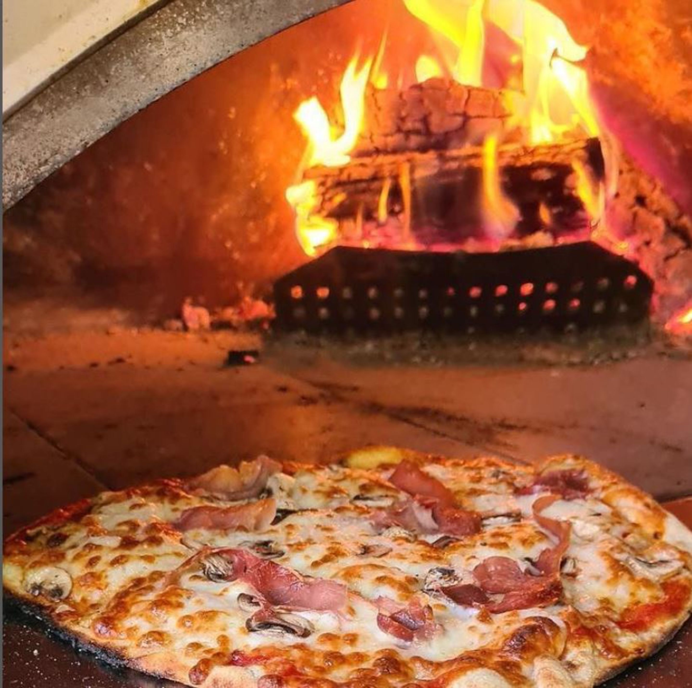 Una pizza dentro de un horno de leña, con llamas visibles en la parte superior.