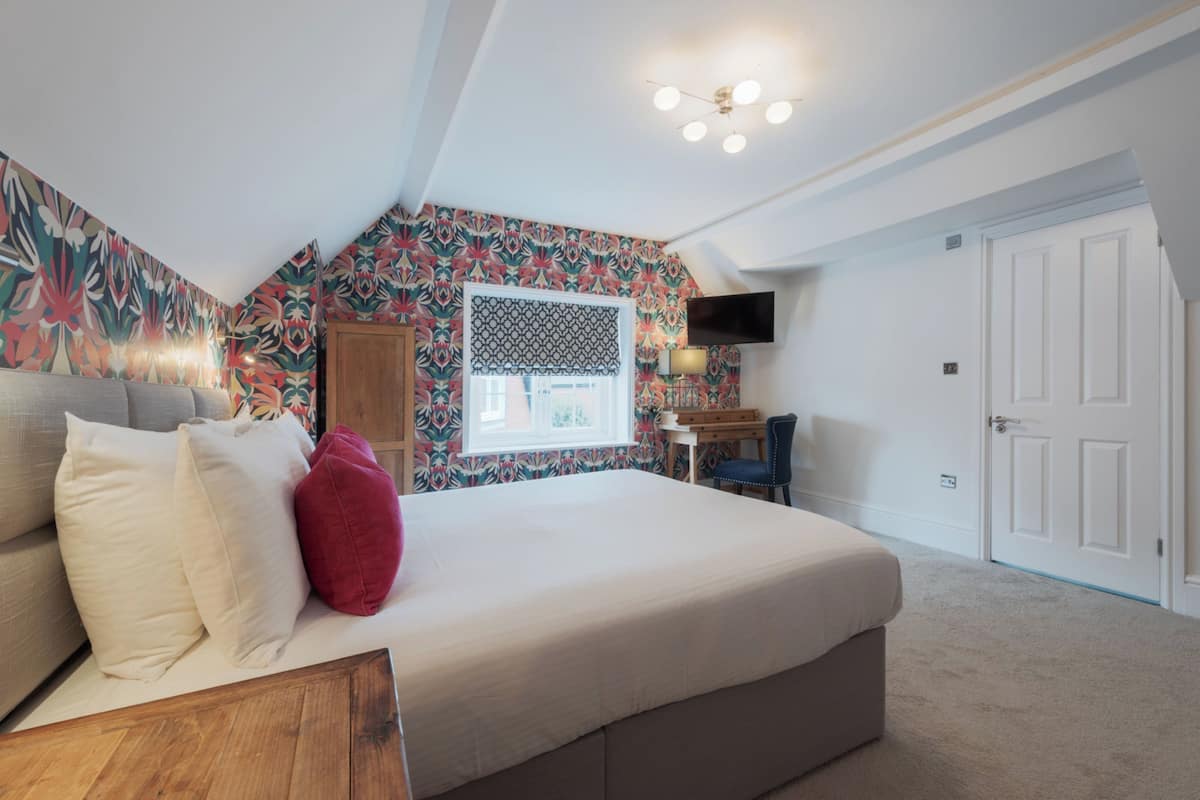 A bedroom with a bed, a desk, a chair, a TV, and a door.