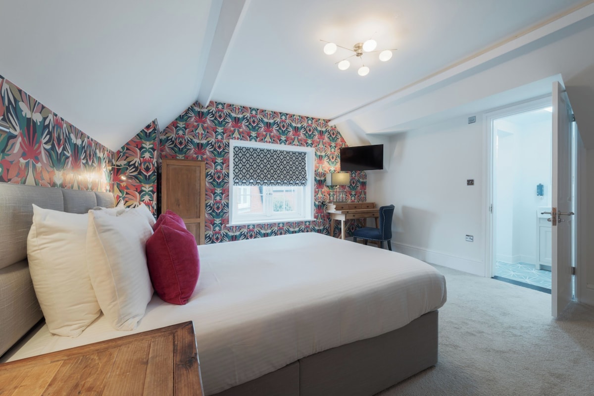 Un dormitorio con cama, escritorio, silla, televisor y ventana.