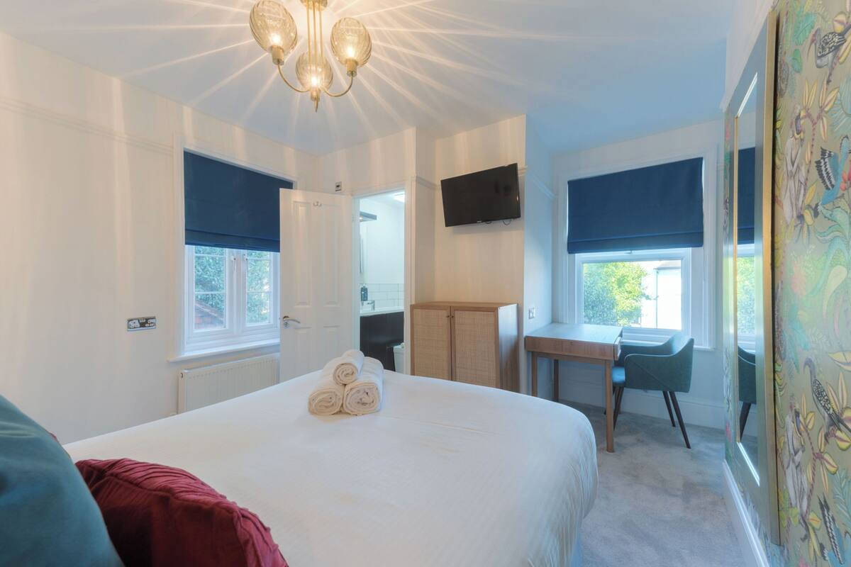 A bedroom with a large bed, a desk, a chair, a TV, and a window with a view.