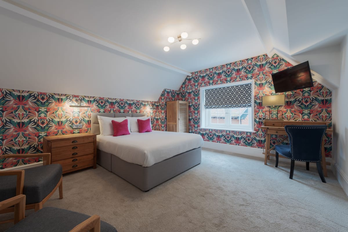 A bedroom with a bed, bedside table, chair, desk, and a TV.