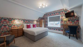 A bedroom with a bed, bedside table, chair, desk, and a TV.
