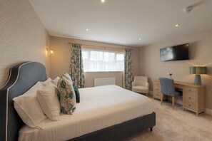 A bedroom with a large bed, a desk, a chair, a television, and a window with curtains. - Florence Suite Hotel & Restaurant (Portsmouth)