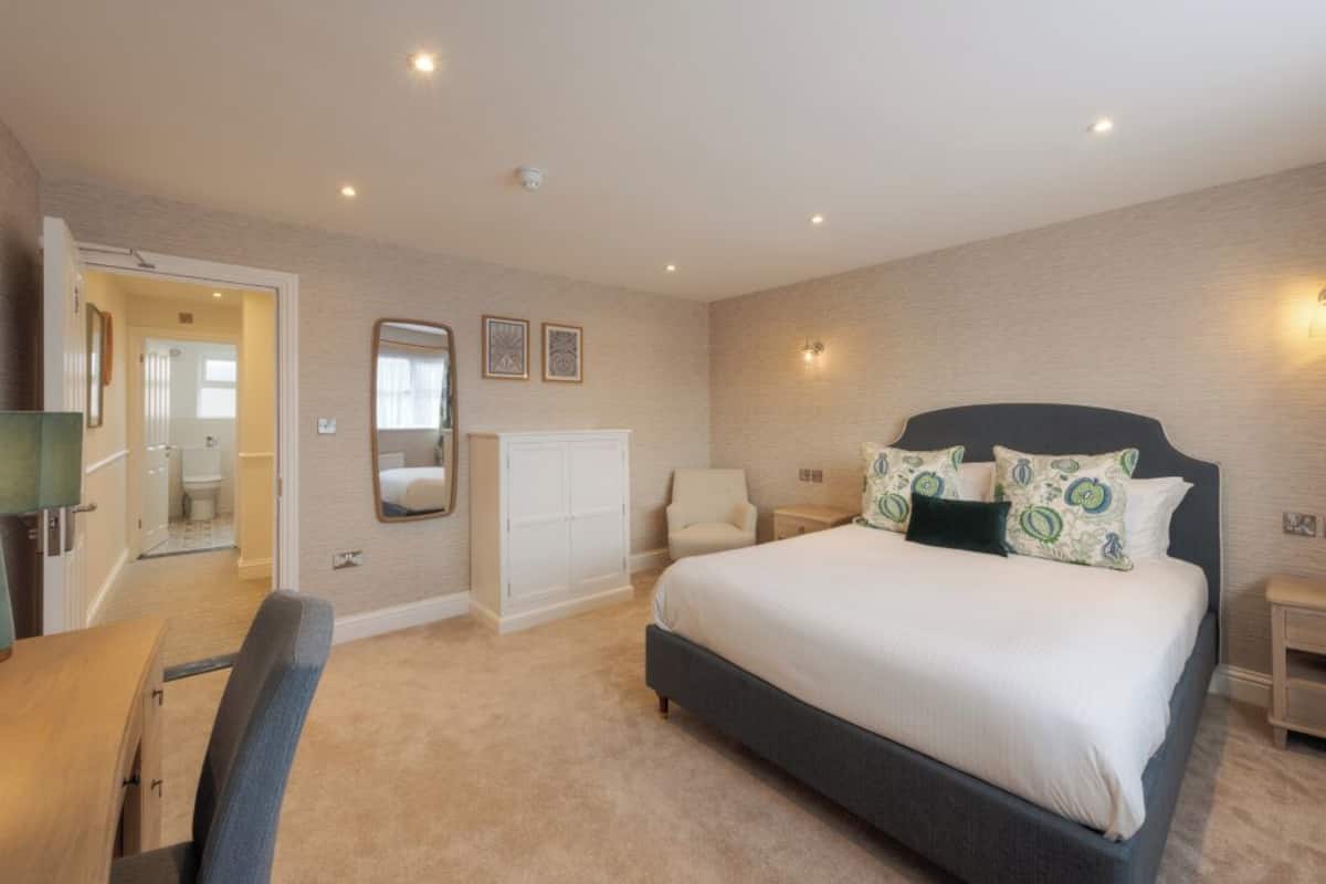A bedroom with a large bed, a desk, a chair, a wardrobe, and a mirror.