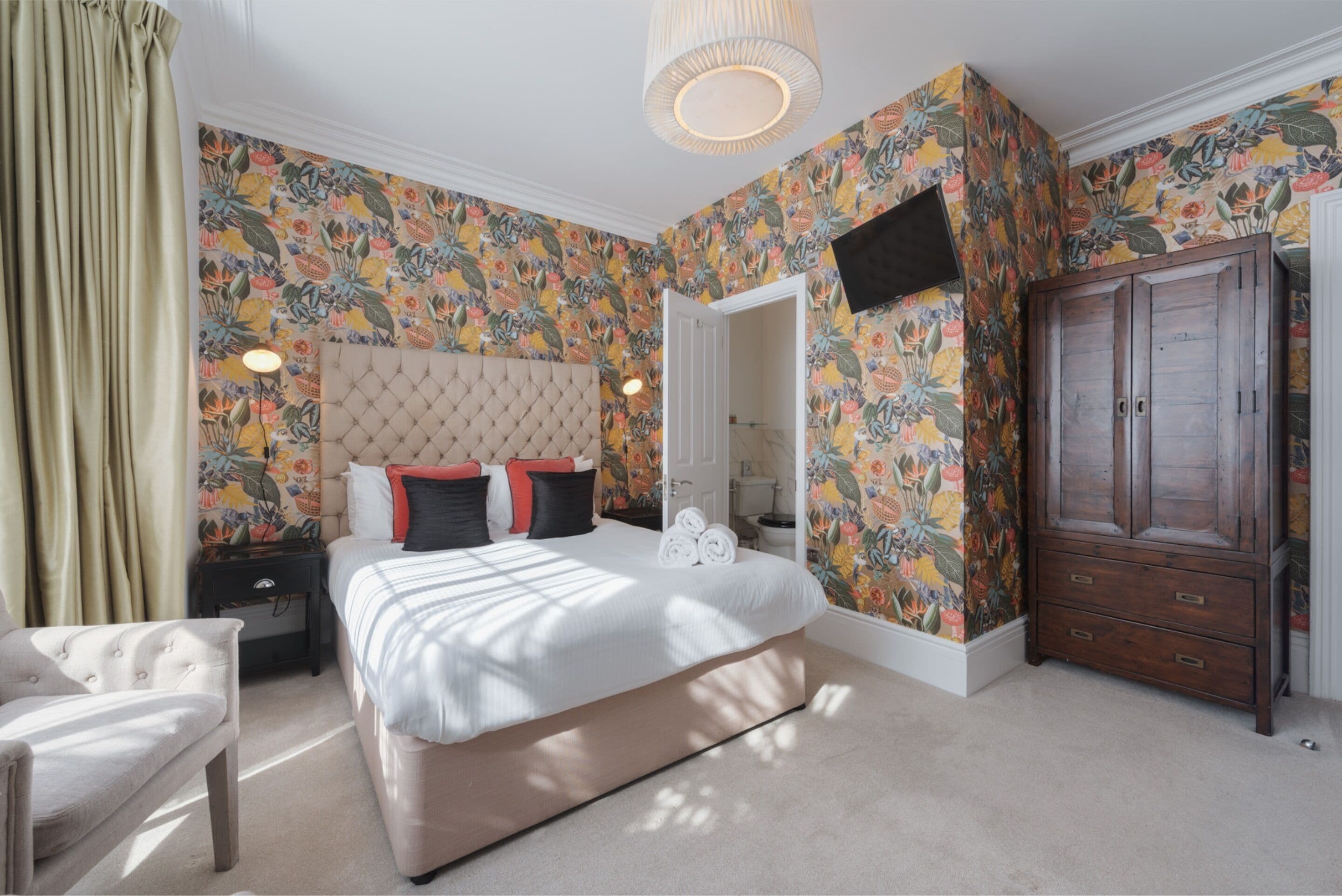 A bedroom with a large bed, a wooden wardrobe, and a floral wallpaper design.
